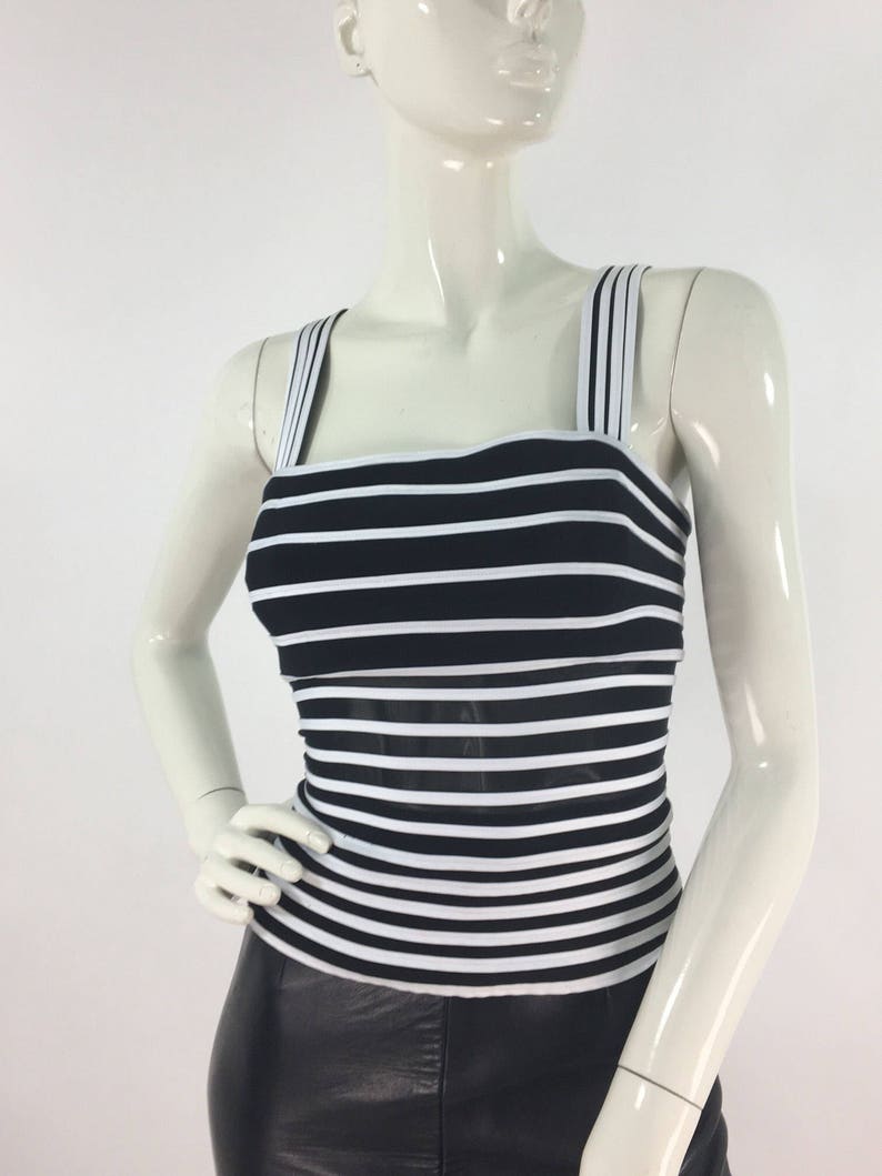 May include: A black and white striped tank top with thin straps. The top is made of a stretchy material and has a fitted silhouette.