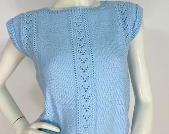 May include: A light blue knitted sleeveless top. The top features a round neckline and a ribbed hem. Decorative openwork detailing runs down the center and along the shoulders. The garment is displayed on a mannequin.