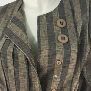 Puede incluir: Una chaqueta de rayas marrones y negras con cierre de botones. La chaqueta tiene cuello y mangas largas.