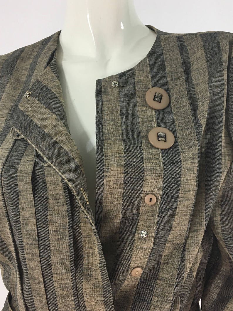 Puede incluir: Una chaqueta de rayas marrones y negras con cierre de botones. La chaqueta tiene cuello y mangas largas.