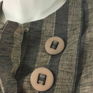 Puede incluir: Primer plano de una chaqueta de tela a rayas con dos botones grandes de color marr&oacute;n. La tela es una mezcla de rayas marrones y negras.