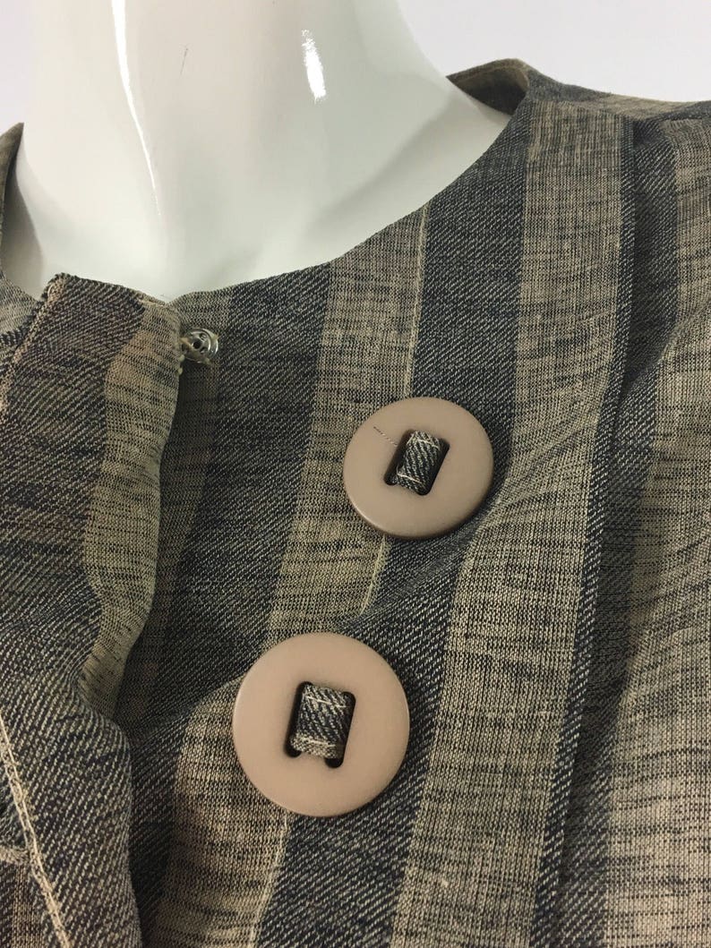 Puede incluir: Primer plano de una chaqueta de tela a rayas con dos botones grandes de color marr&oacute;n. La tela es una mezcla de rayas marrones y negras.