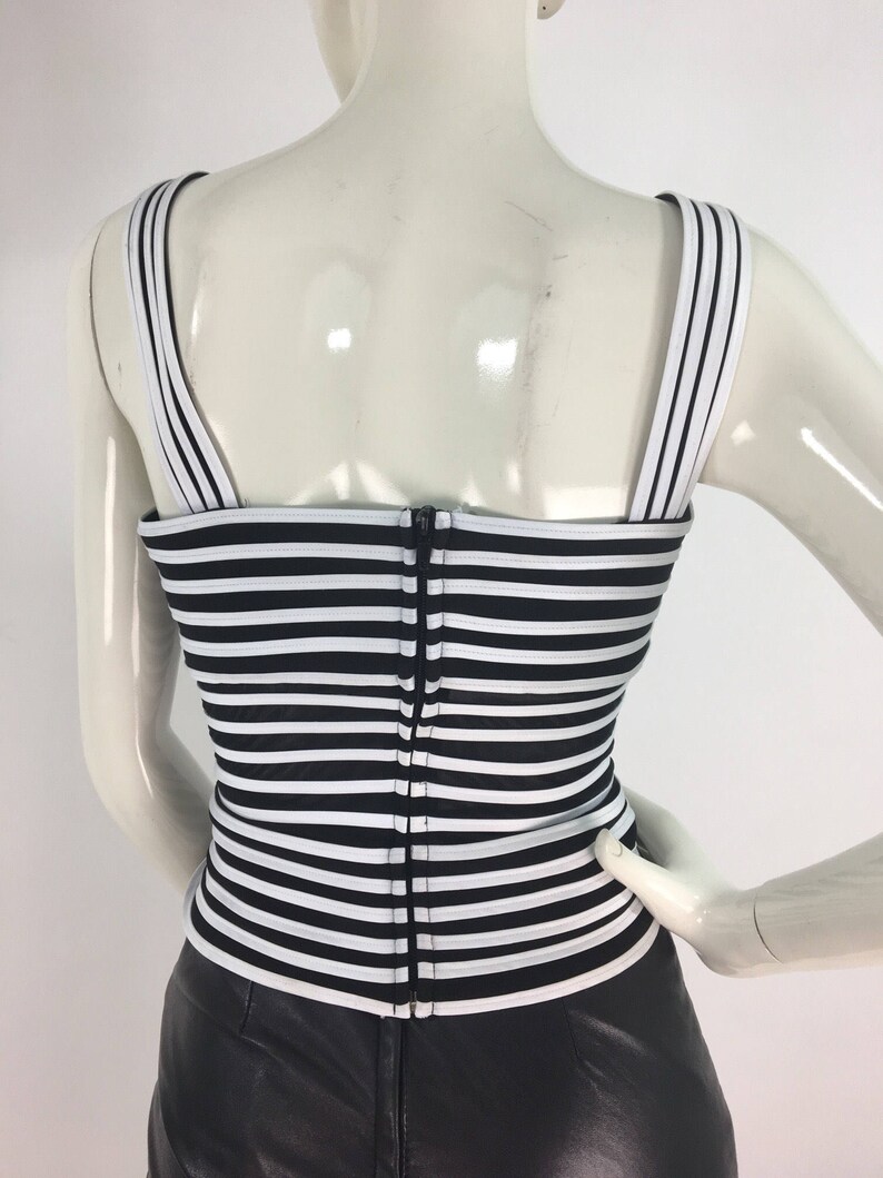 May include: Black and white striped sleeveless top with a zipper closure in the back. The top is made of a stretchy fabric and has a fitted silhouette.
