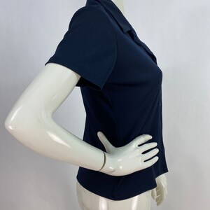 May include: A navy blue short-sleeved collared shirt. The shirt has a button-down front and a tailored fit. The fabric appears to be a smooth, solid color. The shirt is displayed on a mannequin.