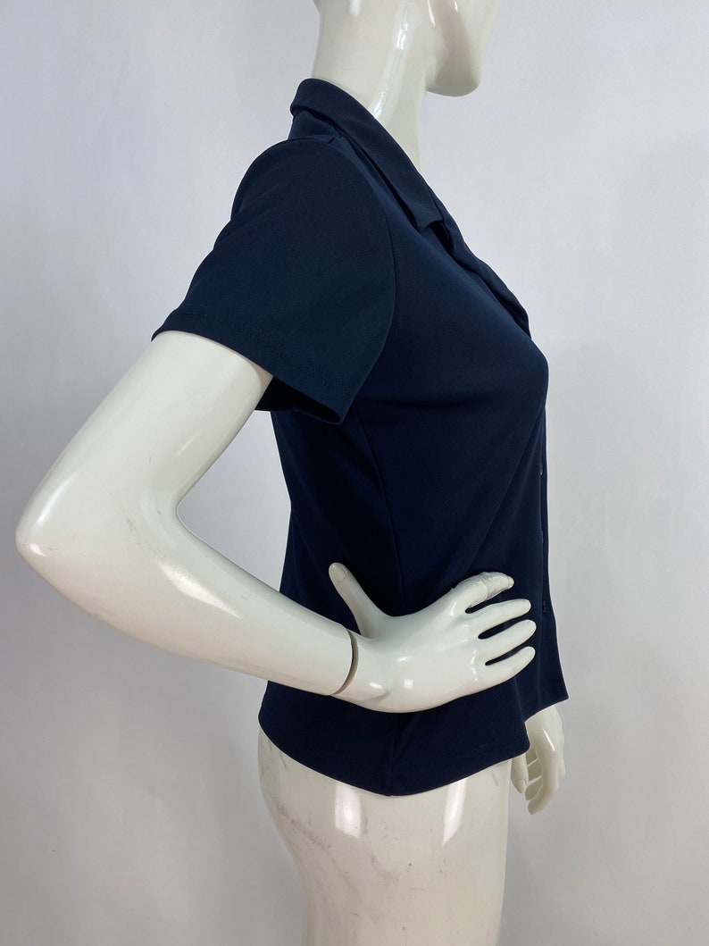 May include: A navy blue short-sleeved collared shirt. The shirt has a button-down front and a tailored fit. The fabric appears to be a smooth, solid color. The shirt is displayed on a mannequin.