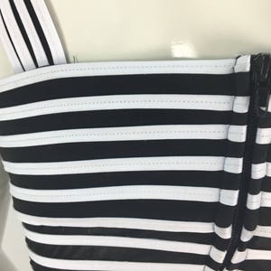 May include: Black and white striped top with a zipper closure. The top has a fitted bodice and a wide, horizontal stripe pattern.