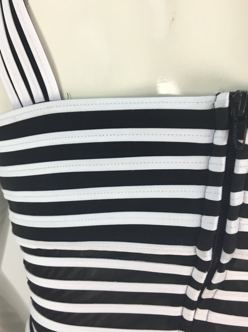 May include: Black and white striped top with a zipper closure. The top has a fitted bodice and a wide, horizontal stripe pattern.