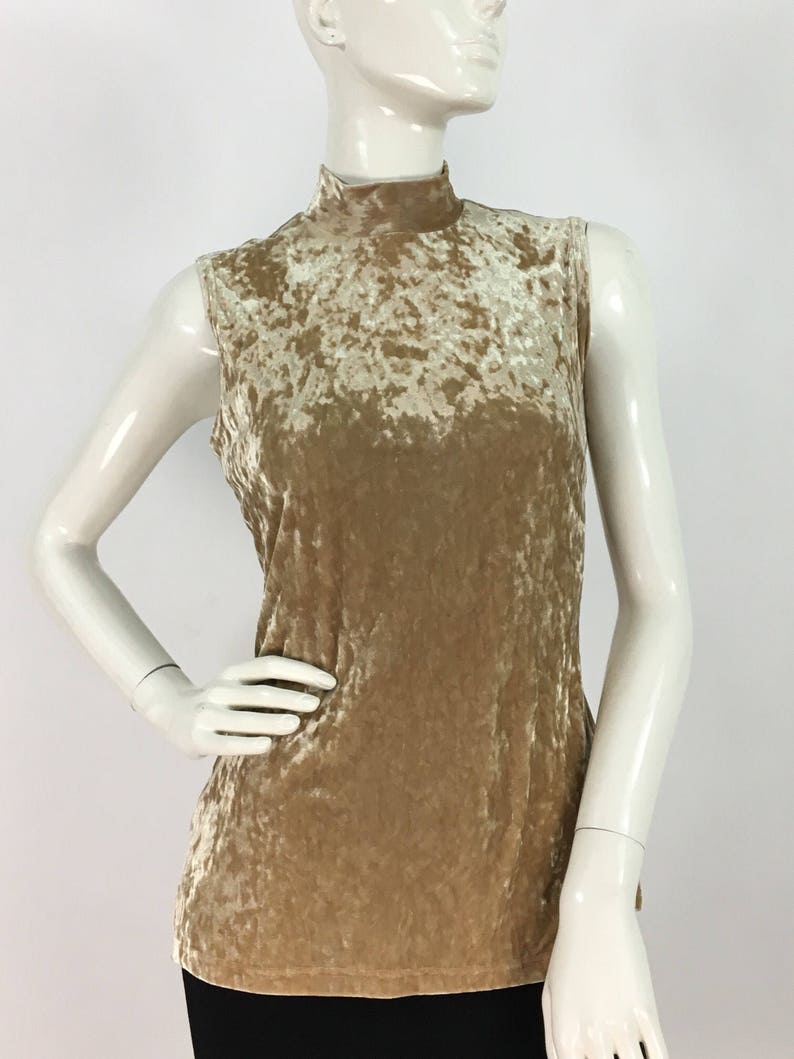 May include: A sleeveless, mock neck top made of crushed velvet in a light beige color.