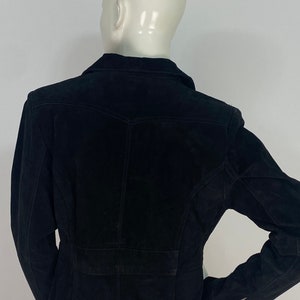 May include: A black suede jacket with a collared neckline and long sleeves. The jacket has a fitted silhouette and a button closure.