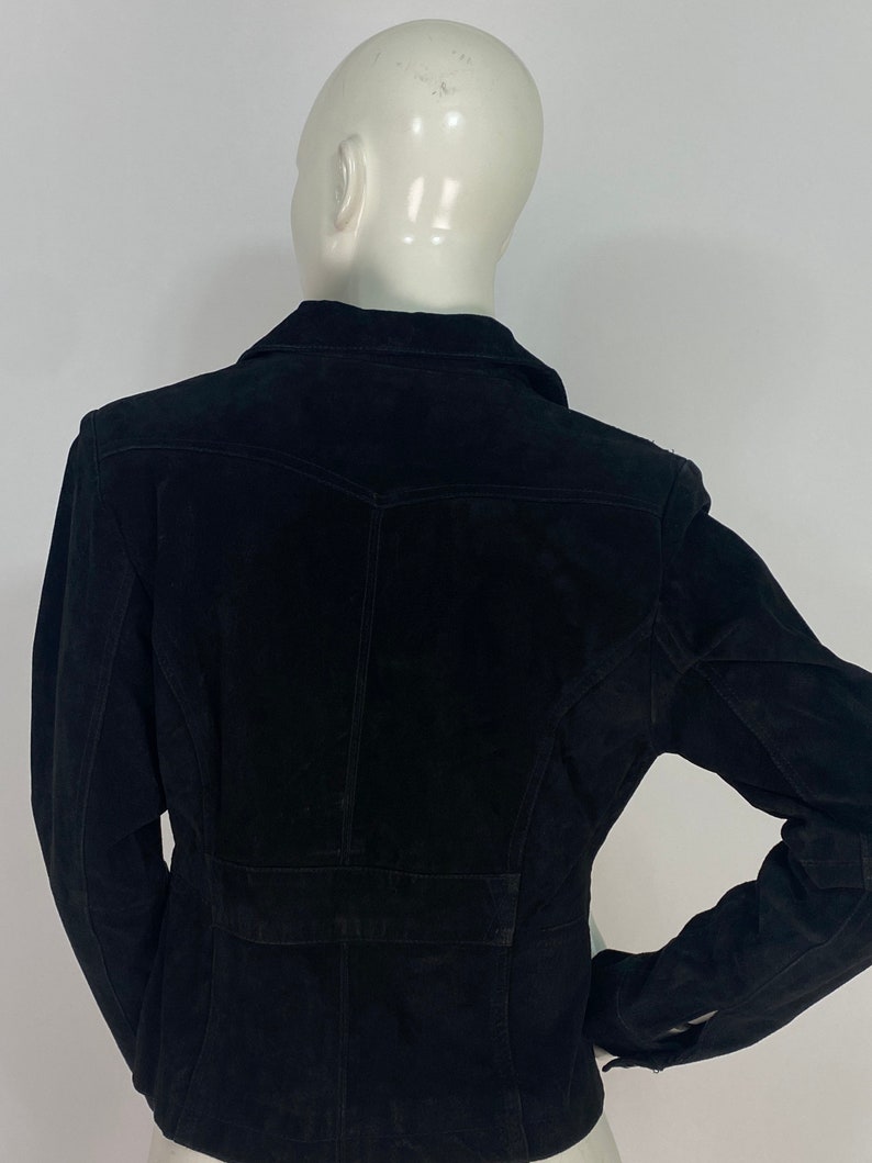 May include: A black suede jacket with a collared neckline and long sleeves. The jacket has a fitted silhouette and a button closure.
