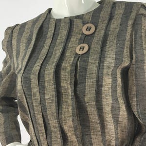 Puede incluir: Un vestido de manga larga a rayas marr&oacute;n y negro con cuello redondo y dos botones marrones.
