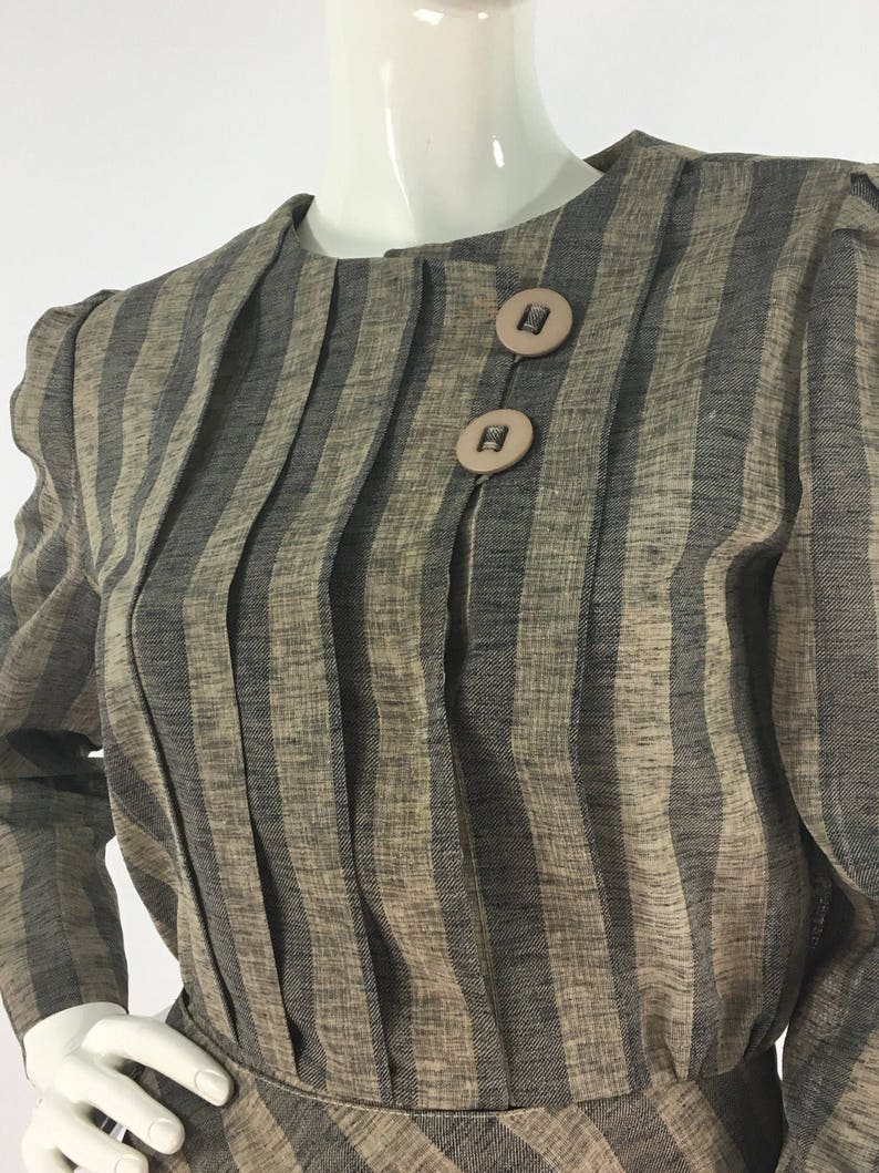Puede incluir: Un vestido de manga larga a rayas marr&oacute;n y negro con cuello redondo y dos botones marrones.