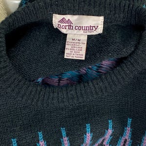 Pode incluir: Camisola preta e azul com padr&atilde;o e uma etiqueta da North Country Eaton. A etiqueta indica que a camisola &eacute; feita de 95% acr&iacute;lico e 5% l&atilde;. A etiqueta tamb&eacute;m indica que a camisola &eacute; feita em Taiwan.