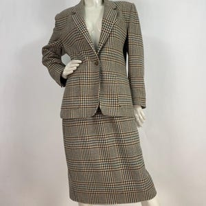 May include: A brown, white and blue plaid skirt suit. The jacket has a single button fastening and a notched collar. The skirt is knee-length.