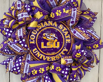 May include: Purple and gold LSU Tigers wreath with a metal sign that reads "Louisiana State University" with the LSU logo and "Est. 1860". The wreath is decorated with purple and gold ribbons, white polka dots, and paw prints.