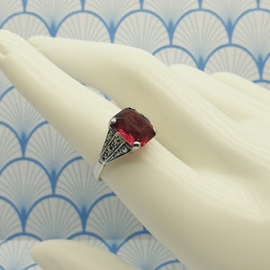 May include: A silver ring featuring a red gemstone and marcasite accents. The ring is displayed against a white background.
