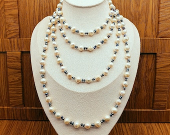 Può includere: Una lunga collana a più fili caratterizzata dall'alternanza di perle d'acqua dolce color crema e piccole perle metalliche grigio scuro. Le perle sono rotonde e di forma irregolare, infilate insieme per creare un effetto a strati su un busto.
