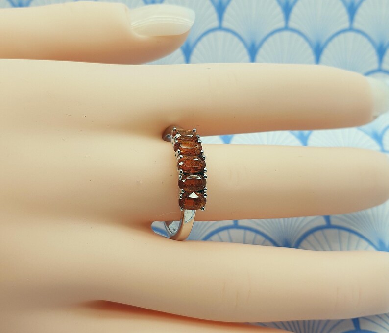 Puede incluir: Un anillo de banda de plata con una fila de piedras preciosas marrones ovaladas.