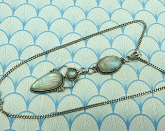 May include: A silver necklace with a pendant featuring three iridescent moonstone cabochons. The pendant has a teardrop shape and two oval stones, all set in ornate silver settings. The chain is a delicate curb link style.