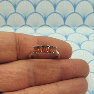 Puede incluir: Un anillo de banda de plata con cinco piedras ovaladas de color naranja.