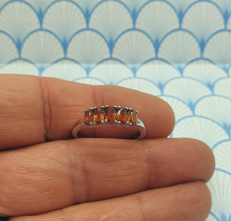Puede incluir: Un anillo de banda de plata con cinco piedras ovaladas de color naranja.