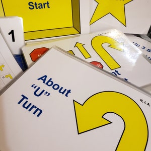 May include: A collection of white cards with yellow and blue text and graphics. The cards include the words "Start", "Finish", and "About 'U' Turn". A yellow arrow and the number "1" are also visible.