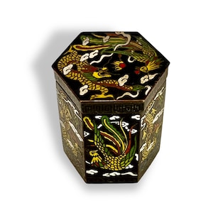 May include: A hexagonal black box with a lid decorated with a colorful dragon and phoenix design. The box is made of metal and has a glossy finish.