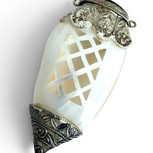May include: A teardrop-shaped pendant featuring a white iridescent shell center with a cut-out lattice pattern. The top and bottom ends are capped with ornate, oxidized silver-tone metal filigree featuring floral and leaf motifs.
