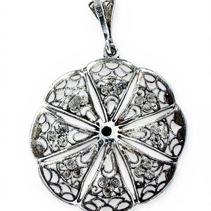 May include: A silver filigree pendant with a floral design. The pendant features an openwork design with intricate details and small, sparkling accents. The pendant has a loop at the top for a chain and is set against a white background.