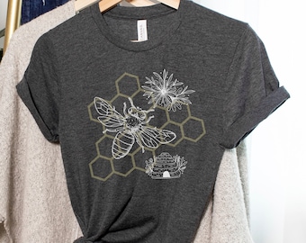 May include: A dark gray t-shirt with a white bee and honeycomb design. The bee is flying near a flower and a beehive.