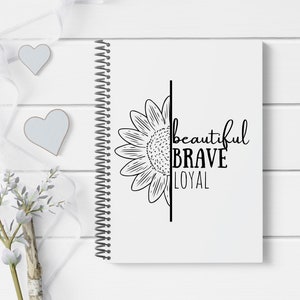 May include: A white spiral bound notebook with a black and white sunflower design and the words "beautiful brave loyal" printed on the cover.