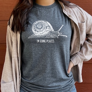 May include: A dark grey t-shirt featuring a white snail graphic and the text "I'm going places".