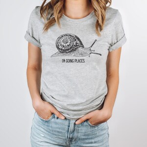 May include: A grey t-shirt with a black and white illustration of a snail and the text "I'm going places".