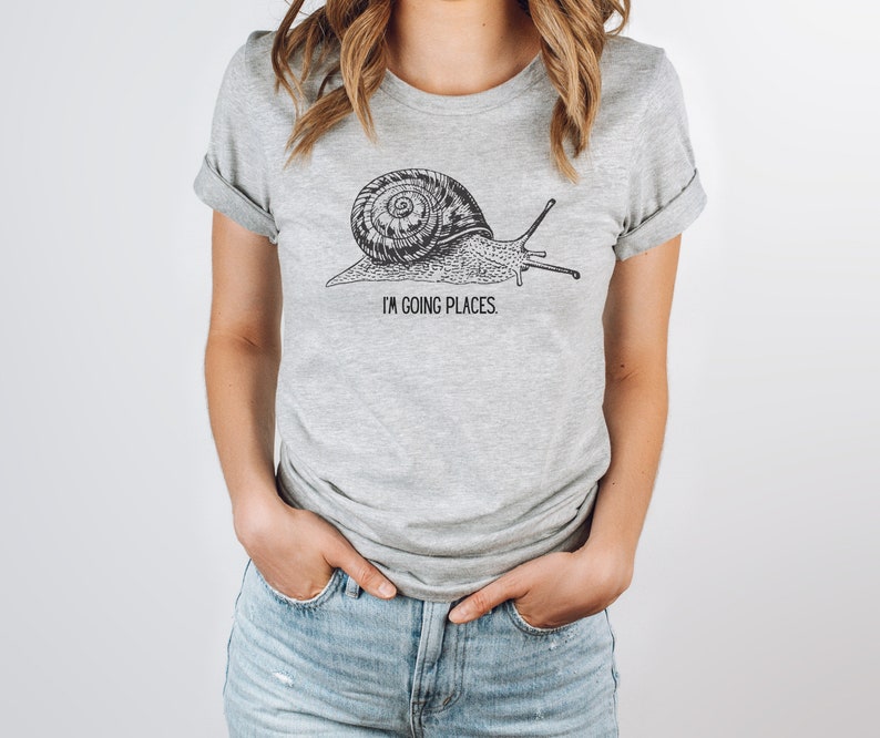 May include: A grey t-shirt with a black and white illustration of a snail and the text "I'm going places".