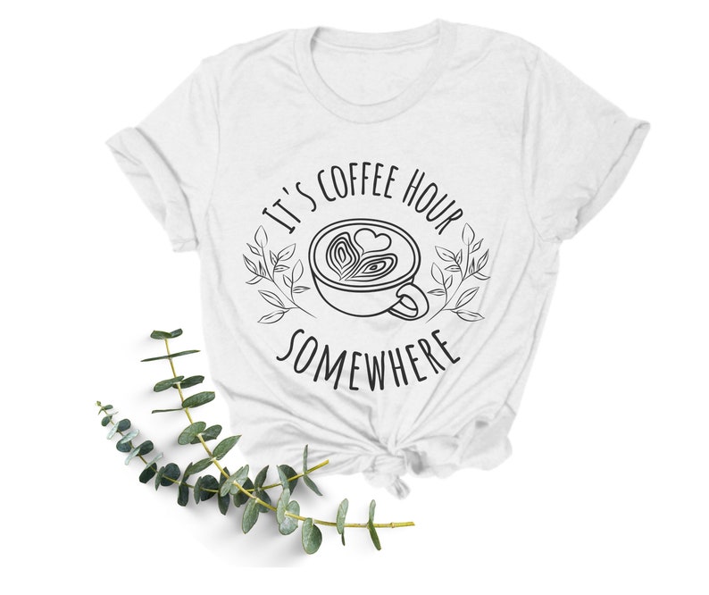May include: White t-shirt with black text that reads "It's coffee hour somewhere" with a stylized drawing of a coffee cup with a heart design.