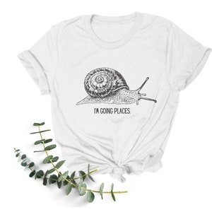 May include: White t-shirt featuring a black and white illustration of a snail with the text "I'm going places."