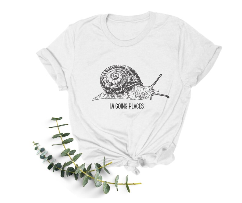 May include: White t-shirt featuring a black and white illustration of a snail with the text "I'm going places."