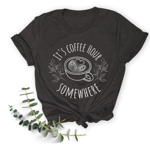 May include: A dark gray t-shirt with the text "It's coffee hour somewhere" and a stylized image of a coffee cup with a heart design.