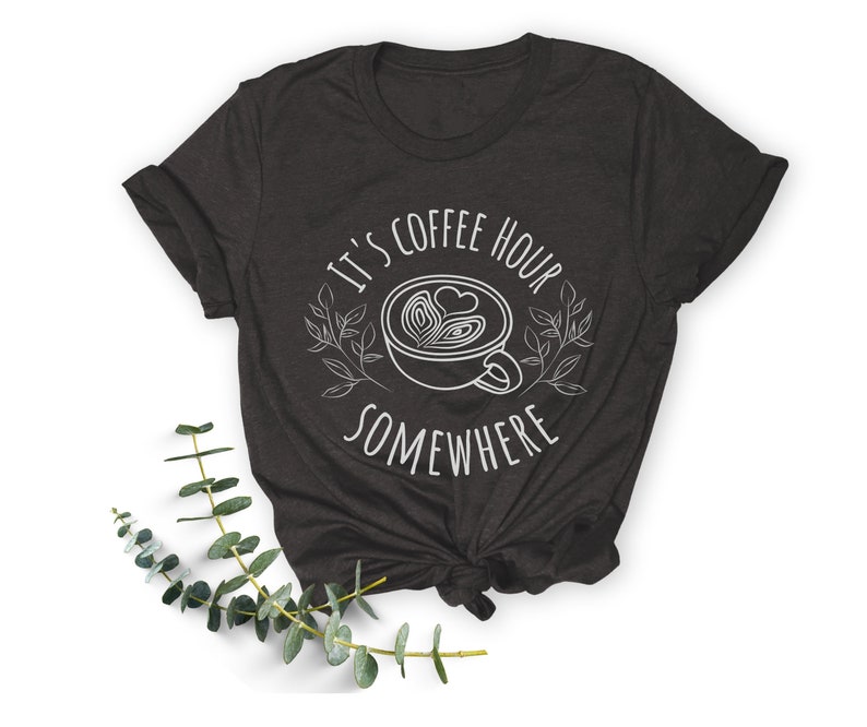 May include: A dark gray t-shirt with the text "It's coffee hour somewhere" and a stylized image of a coffee cup with a heart design.
