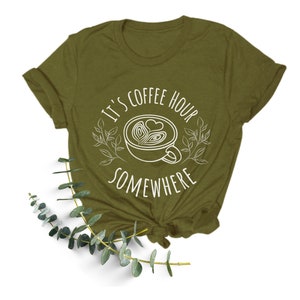 May include: A green t-shirt with a white graphic that says "It's coffee hour somewhere" with a stylized coffee cup and leaves.
