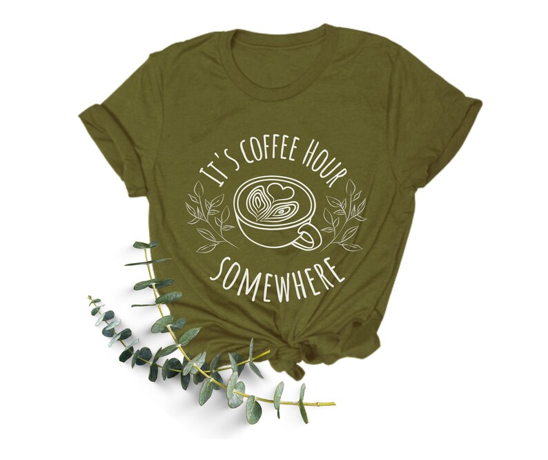 May include: A green t-shirt with a white graphic that says "It's coffee hour somewhere" with a stylized coffee cup and leaves.