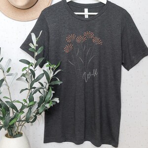 May include: A dark gray t-shirt with a white outline of a flower with orange centers and the word "Wild" printed below the flower.