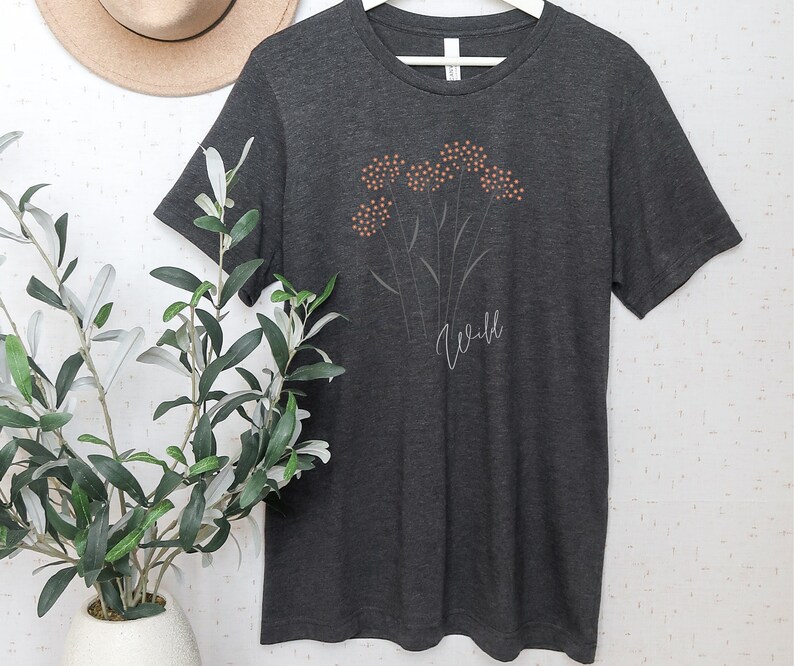 May include: A dark gray t-shirt with a white outline of a flower with orange centers and the word "Wild" printed below the flower.