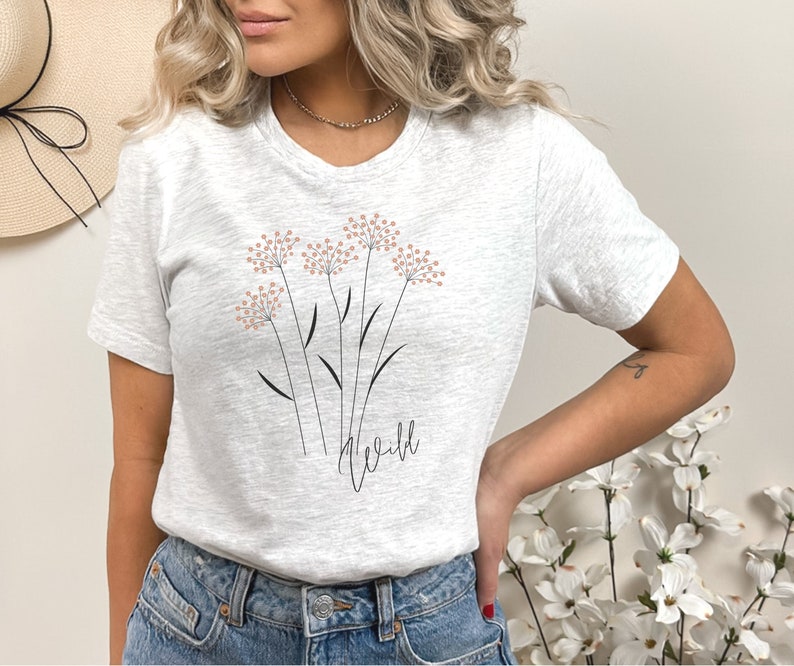 May include: A white t-shirt with a graphic of pink flowers and the word "wild" in black script.