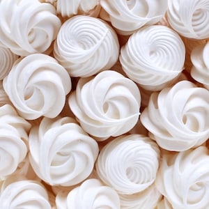 May include: An overhead shot of a collection of white, swirled meringues. Each meringue has a spiral design, with a smooth, glossy texture. The meringues are arranged closely together, filling the frame.