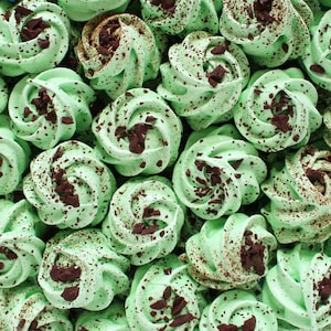 May include: A close-up of a plate of green and brown meringue cookies. The cookies are topped with chocolate shavings.