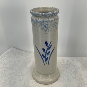 May include: A tall, cylindrical vase with a speckled, off-white finish. The vase features a blue floral design around the rim and a stylized blue wheat stalk motif. The vase has a round base.