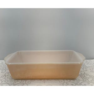 May include: A rectangular, light orange baking dish with rounded corners and two handles. The dish is made of glass and has a smooth, glossy finish. It is empty and ready for use.