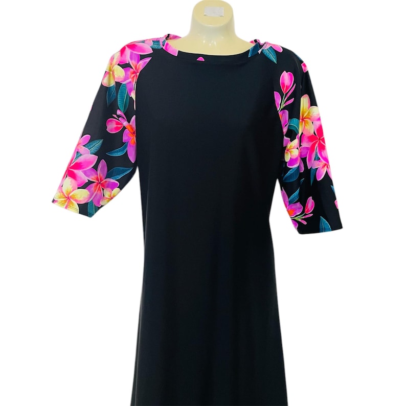Puede incluir: Vestido negro con estampado floral en las mangas. Las mangas son de tres cuartos y el vestido tiene un escote redondo.