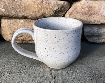 May include: A white ceramic mug with a speckled glaze. The mug has a rounded body and a handle.